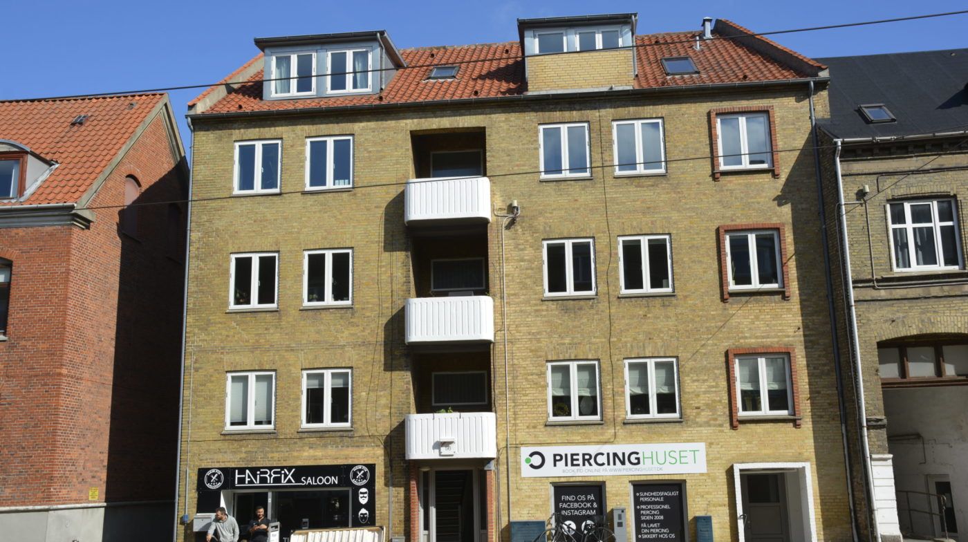 Afbilledet er et tre etagers bygning med fire lejligheder og en butik med teksten Harfix Saloon