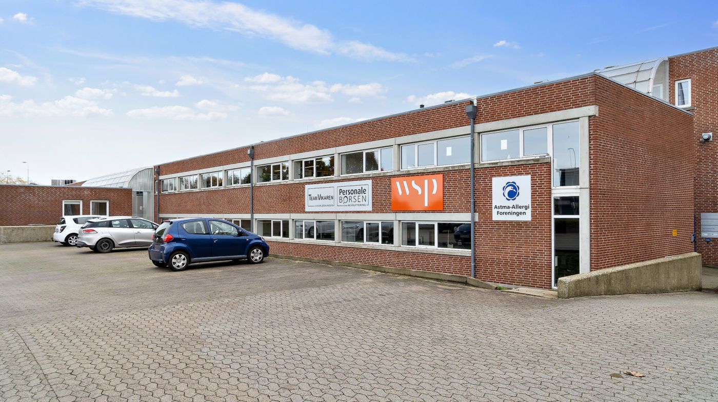 En bygning med flere biler parkeret og skilte med teksten "Personlige Borsen" og "Astma-Allergi Forening"