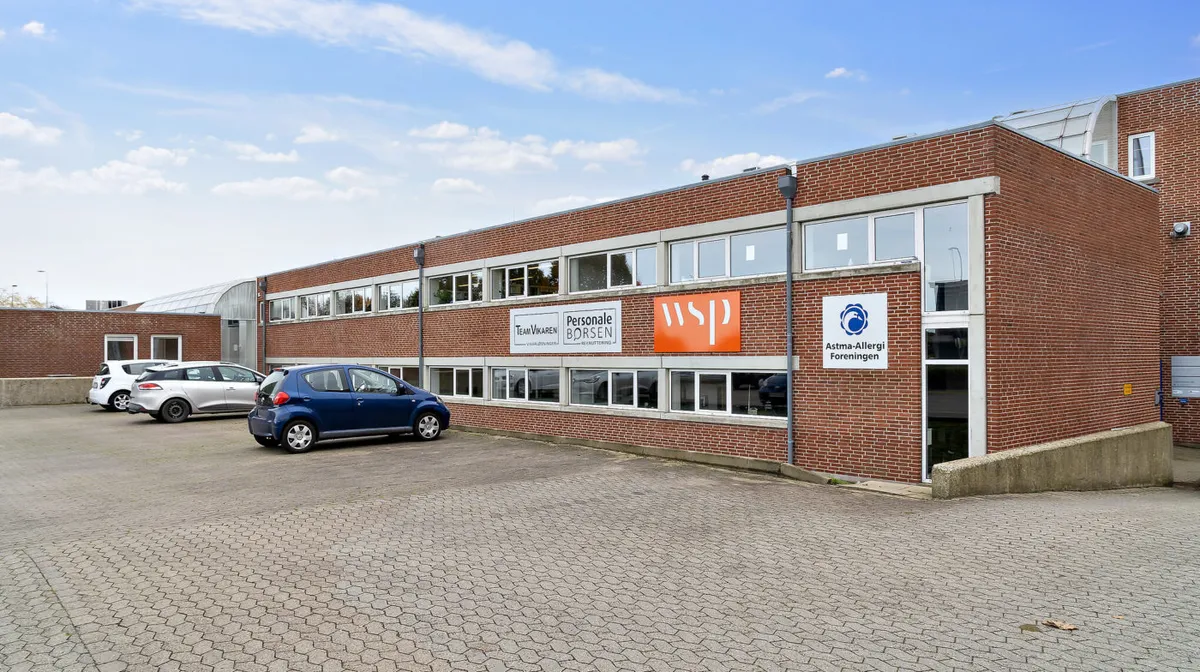 En bygning med flere biler parkeret og skilte med teksten "Personlige Borsen" og "Astma-Allergi Forening"