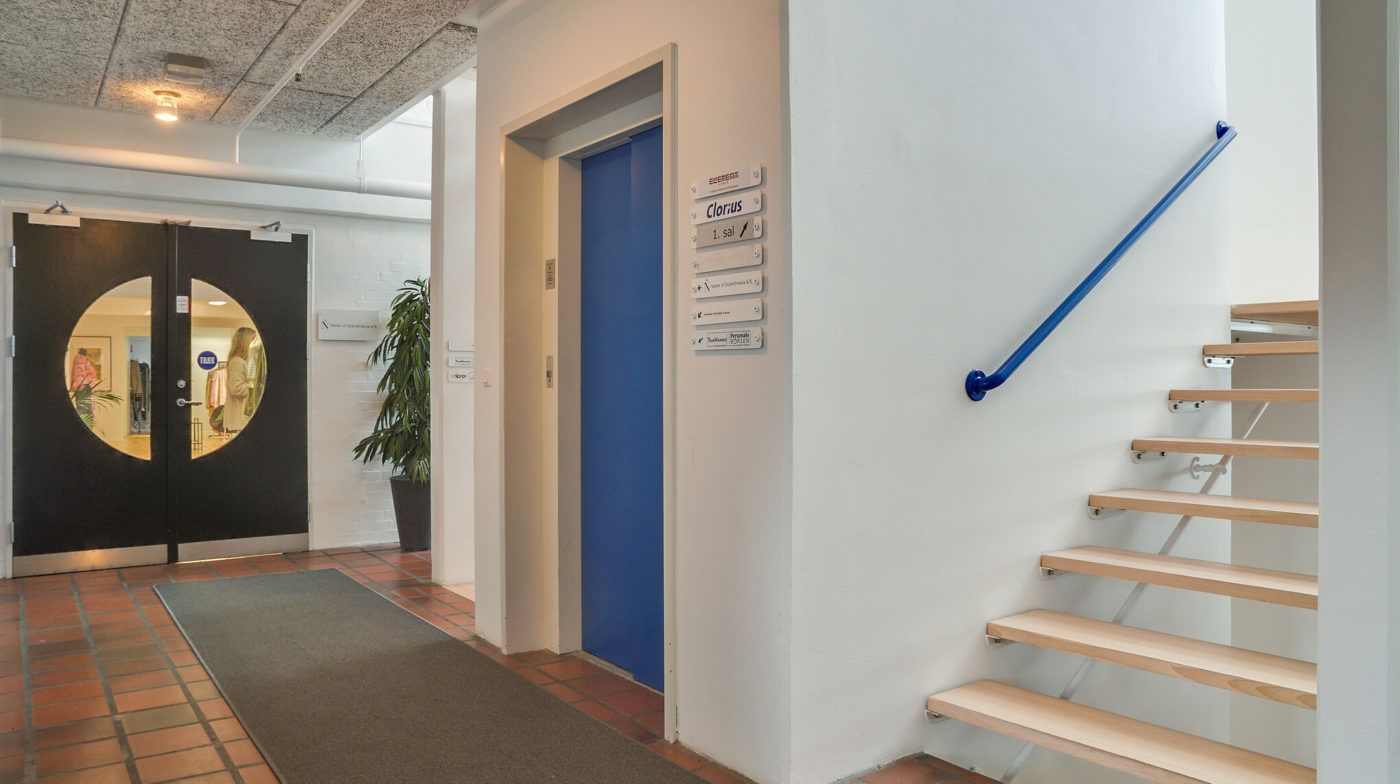 Kontorbygning med lyse møbler og trappe med håndtag, indgangsdøre og gulvbelægning af røde og gule teglsten samt hvid væg