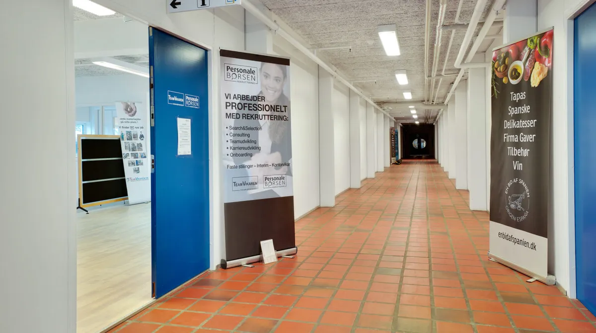 Indenfor et lejet kontor findes reklamebannere og et spejl. Der er også et rekrutteringsbanner med en kvinde og en tekst.