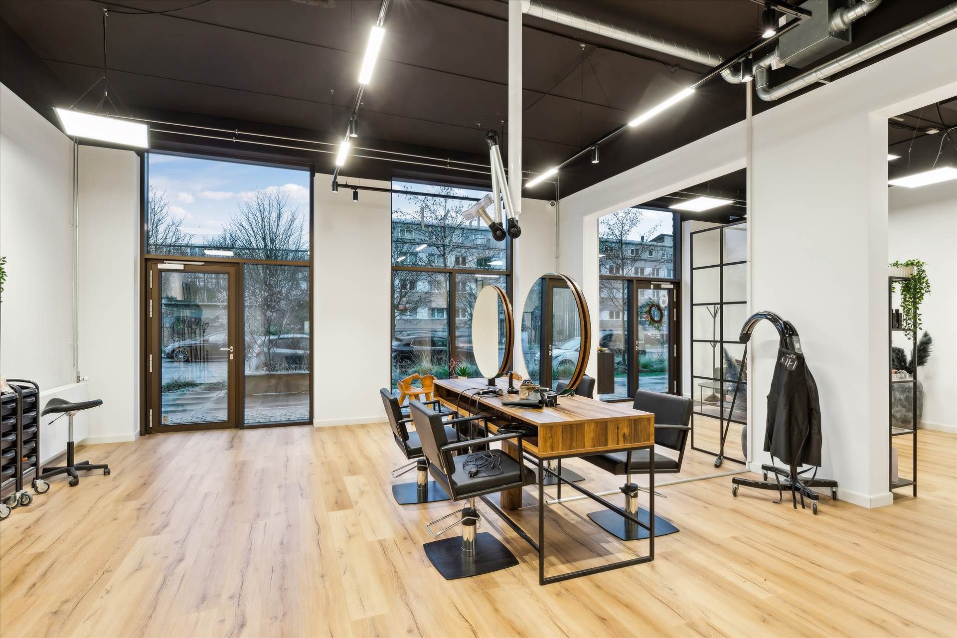 En moderne frisørsalon med lyse gulvbelægning, store vinduer og lysekroner i loftet, der reflekterer på spejle