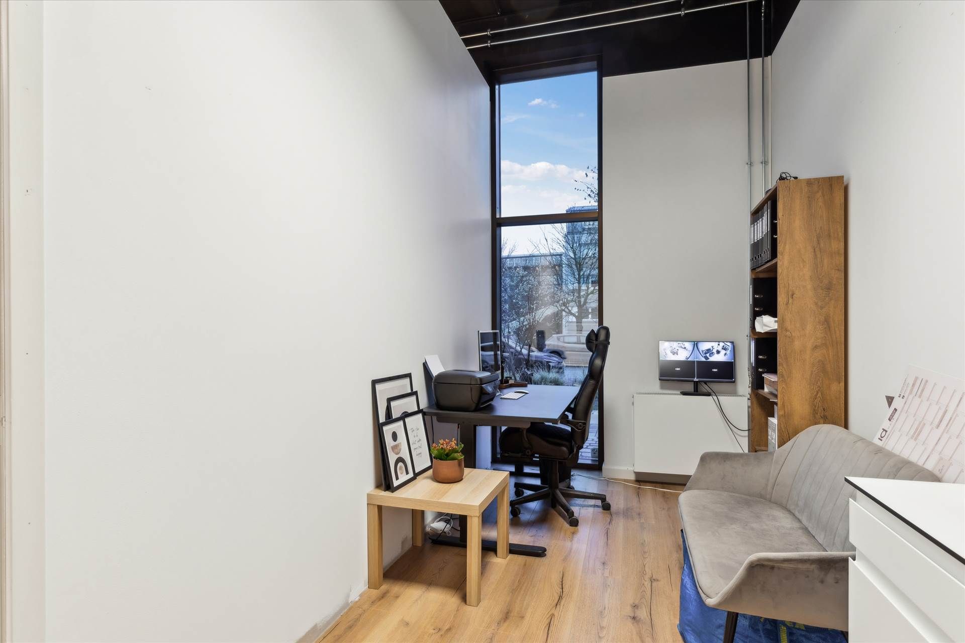 Billede af et moderne kontor med en stor vindue med udsigt til gade og bygninger samt en borde med en computer og printer