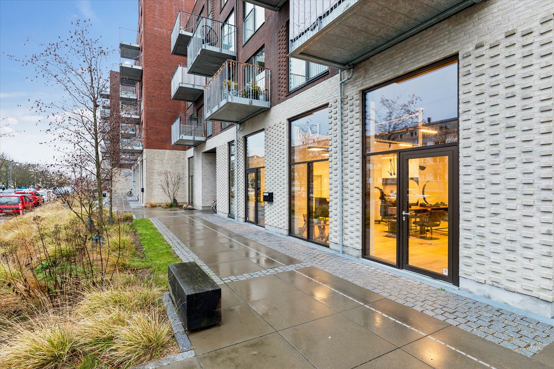 Moderne bygning med glasvinduer, terrasser og parkeringsplads. Lejlighederne er indrettet med minimalistisk design og