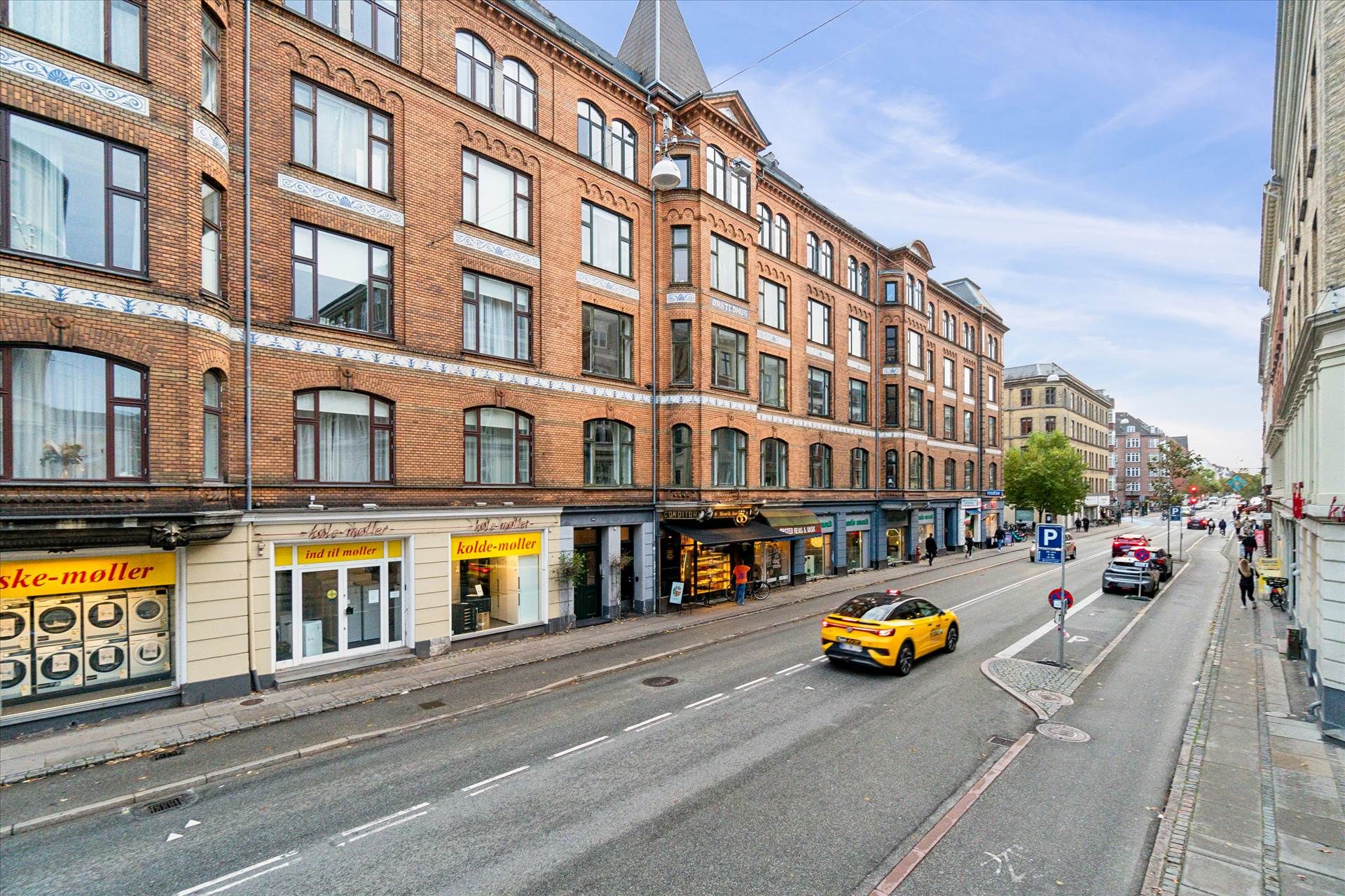 Rækkehus med bageri og forretninger på H.C. Ørsteds Vej i Frederiksberg. En hvid bil kører langs vejen med flere parkerede