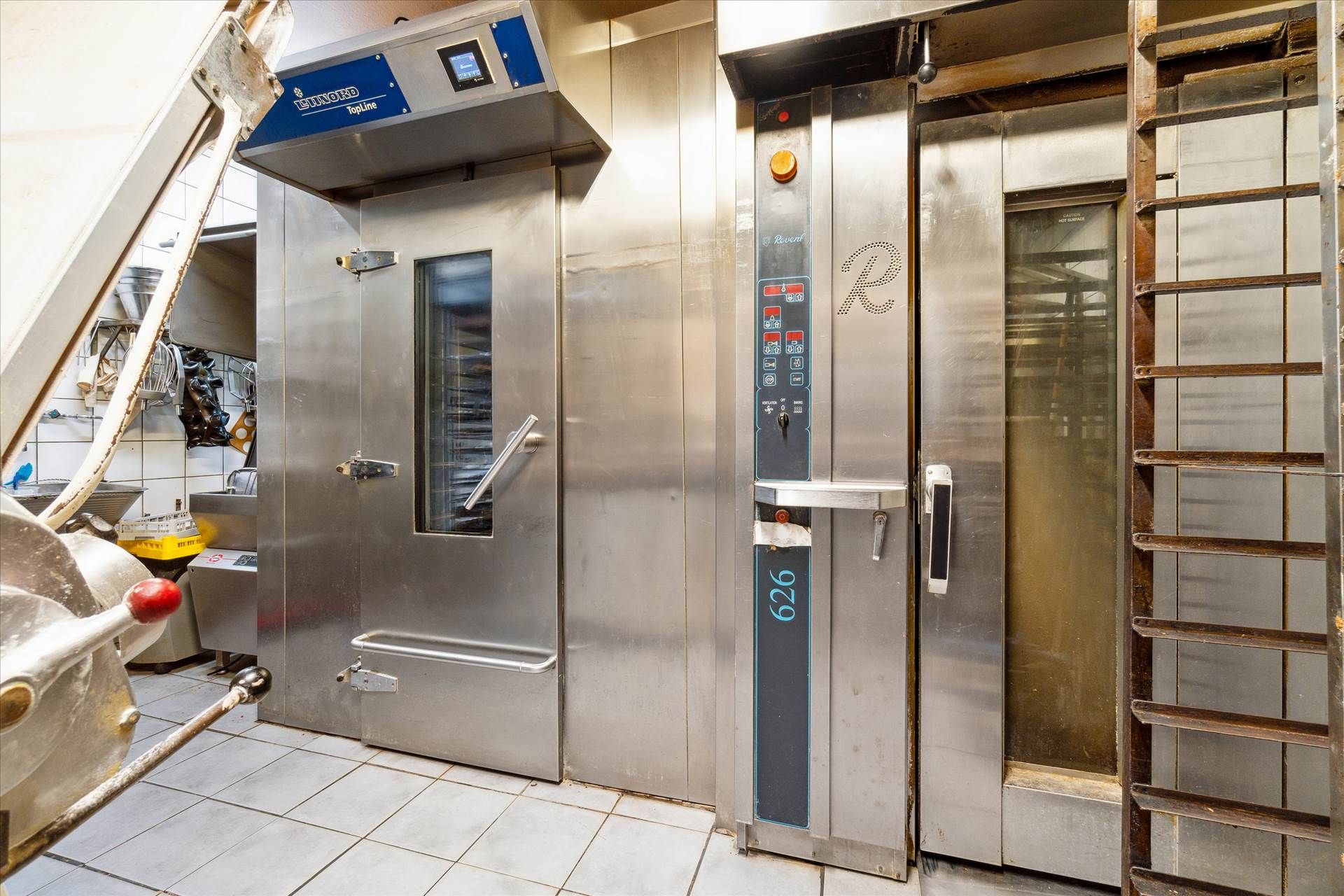 Bageri med moderne ovne, rustfrit stål og teknologiske apparater til madlavning og bagning, en gulv med flise og skabe