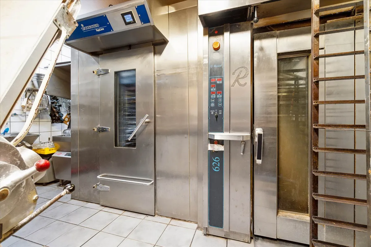 Bageri med moderne ovne, rustfrit stål og teknologiske apparater til madlavning og bagning, en gulv med flise og skabe