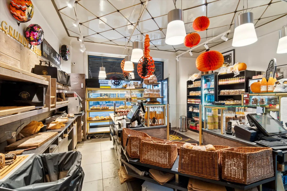 Køkkenborde med bagværk og krydsfinerhyller. Dekoreret loft og gulv. Indkøbskurve med brød og trækasser med emballage.