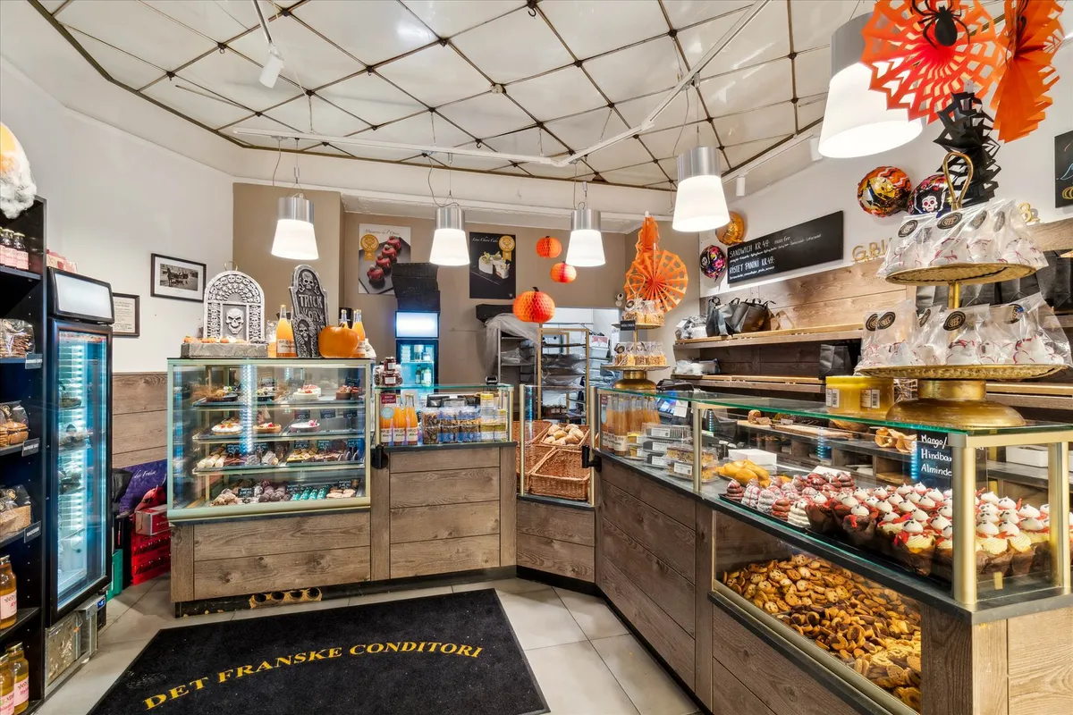 Søde varer som kager og muffins er udstillet i et bageri i flere skufhylder. I samme lokale er der flere køleskabe og en væg