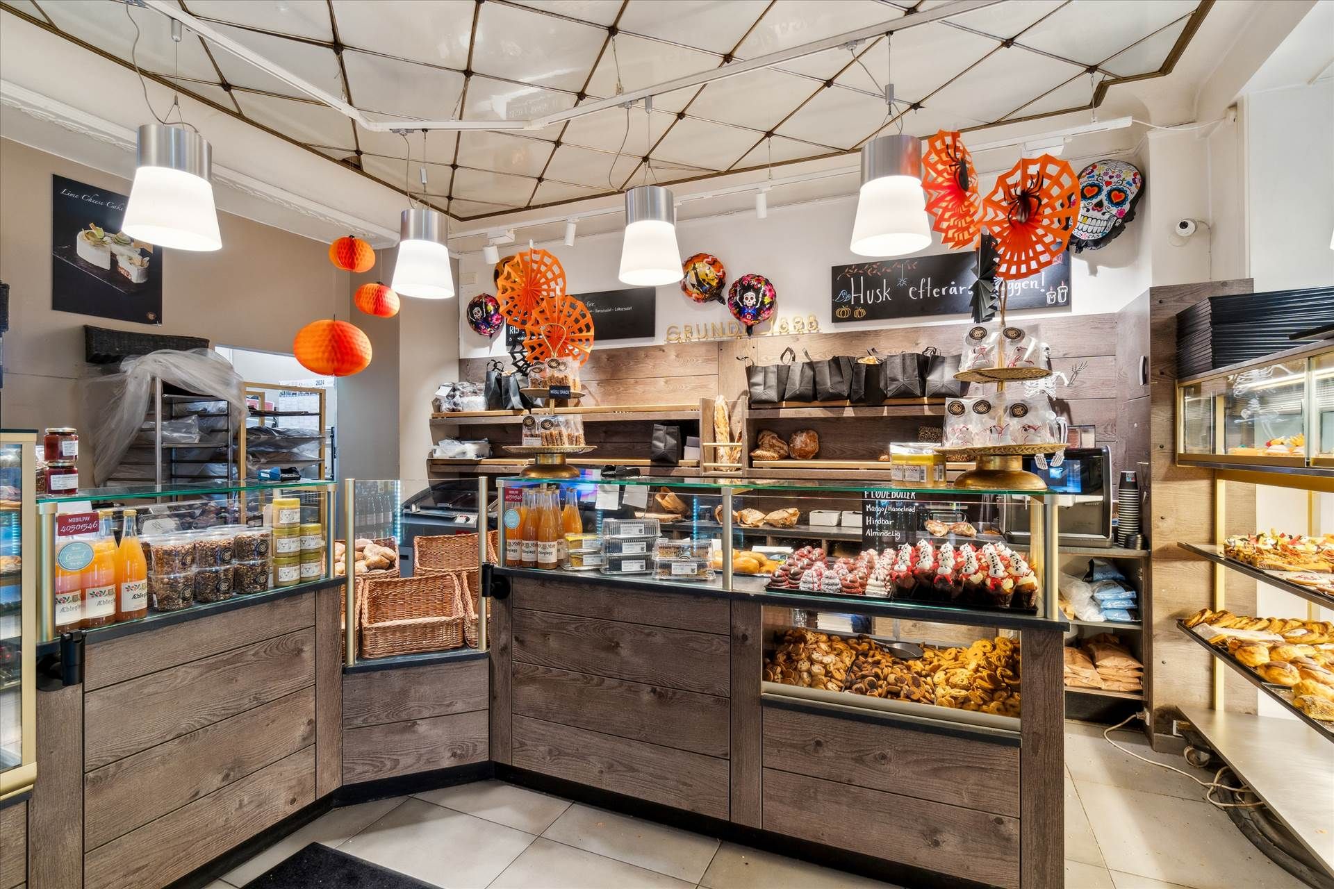 Et bageri med flere salgsdiske, udskårne cookies, kaker, chokolade og trækasser med håndtasker, orange og andre drikkevarer