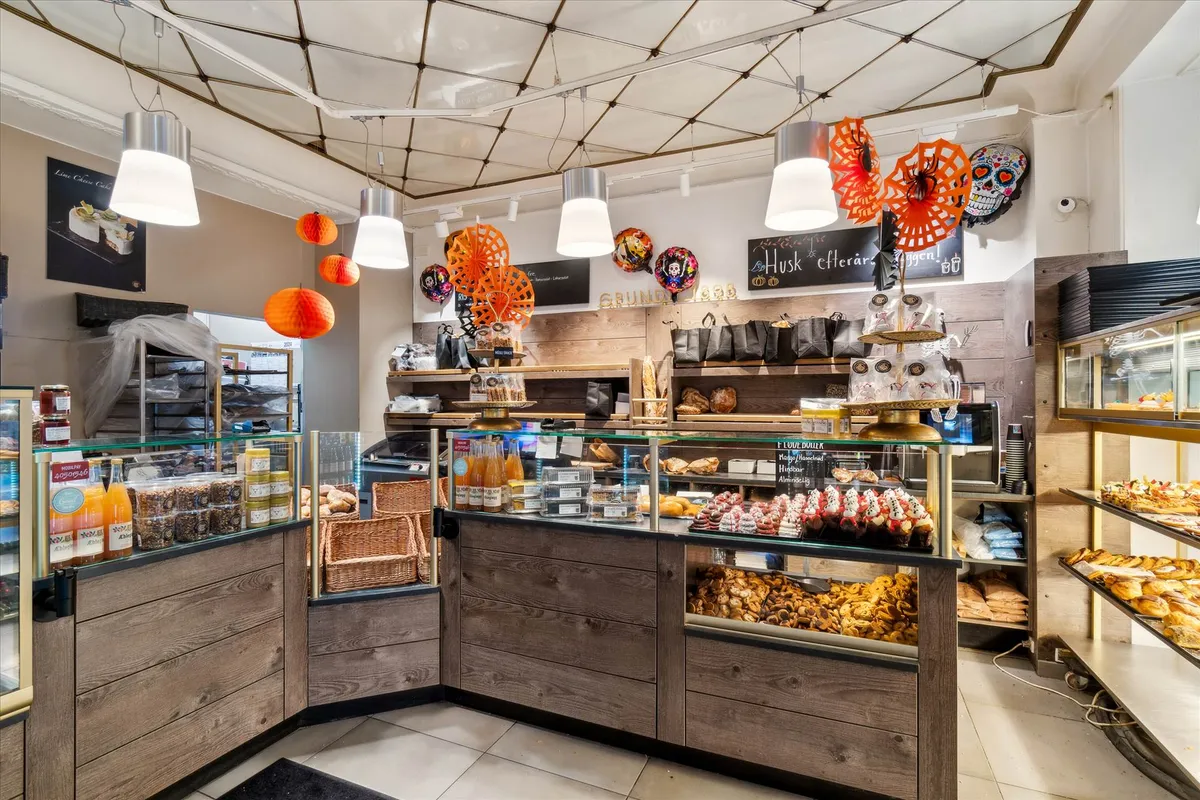 Et bageri med flere salgsdiske, udskårne cookies, kaker, chokolade og trækasser med håndtasker, orange og andre drikkevarer