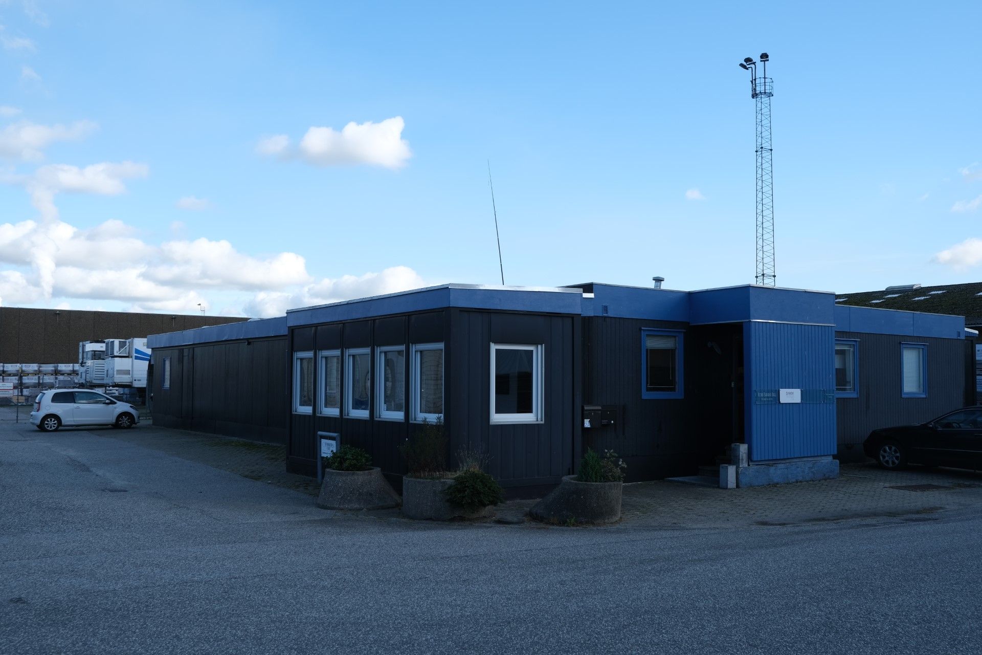 To biler parkeret ved en blå bygning med flere vinduer og plantekasser med grønne planter