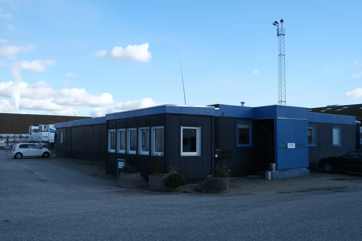 To biler parkeret ved en blå bygning med flere vinduer og plantekasser med grønne planter