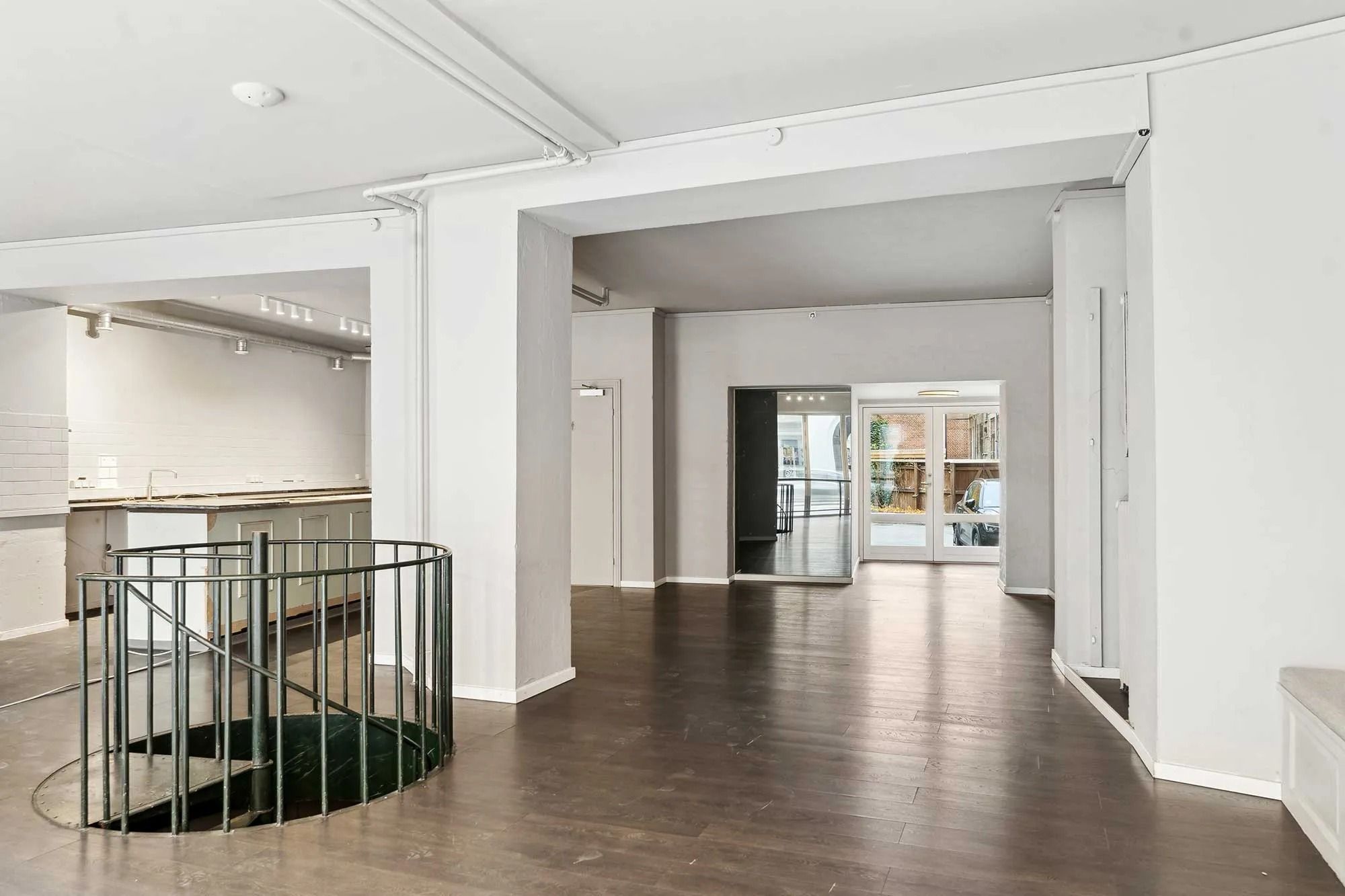 Rummelig stueetage med højloft og åben stue i minimalistisk stil. Loftet er hvidt, og gulvet er lavet af træ. Der er et