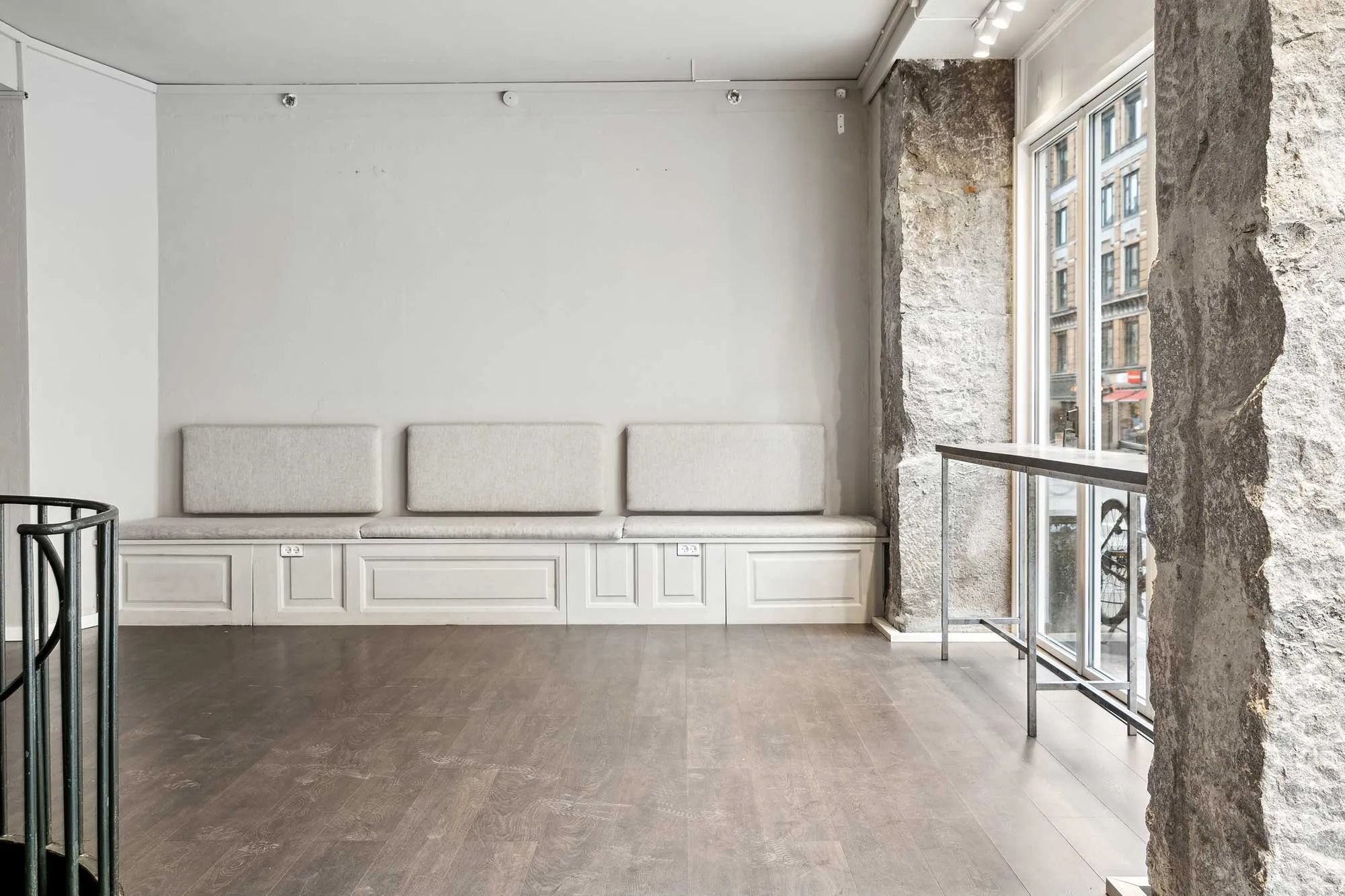 En indre lejlighed med lyse, trægulve og hvide vægge. Møblerne er minimalistiske, og der er et sæt høje bænke med lysepuder.