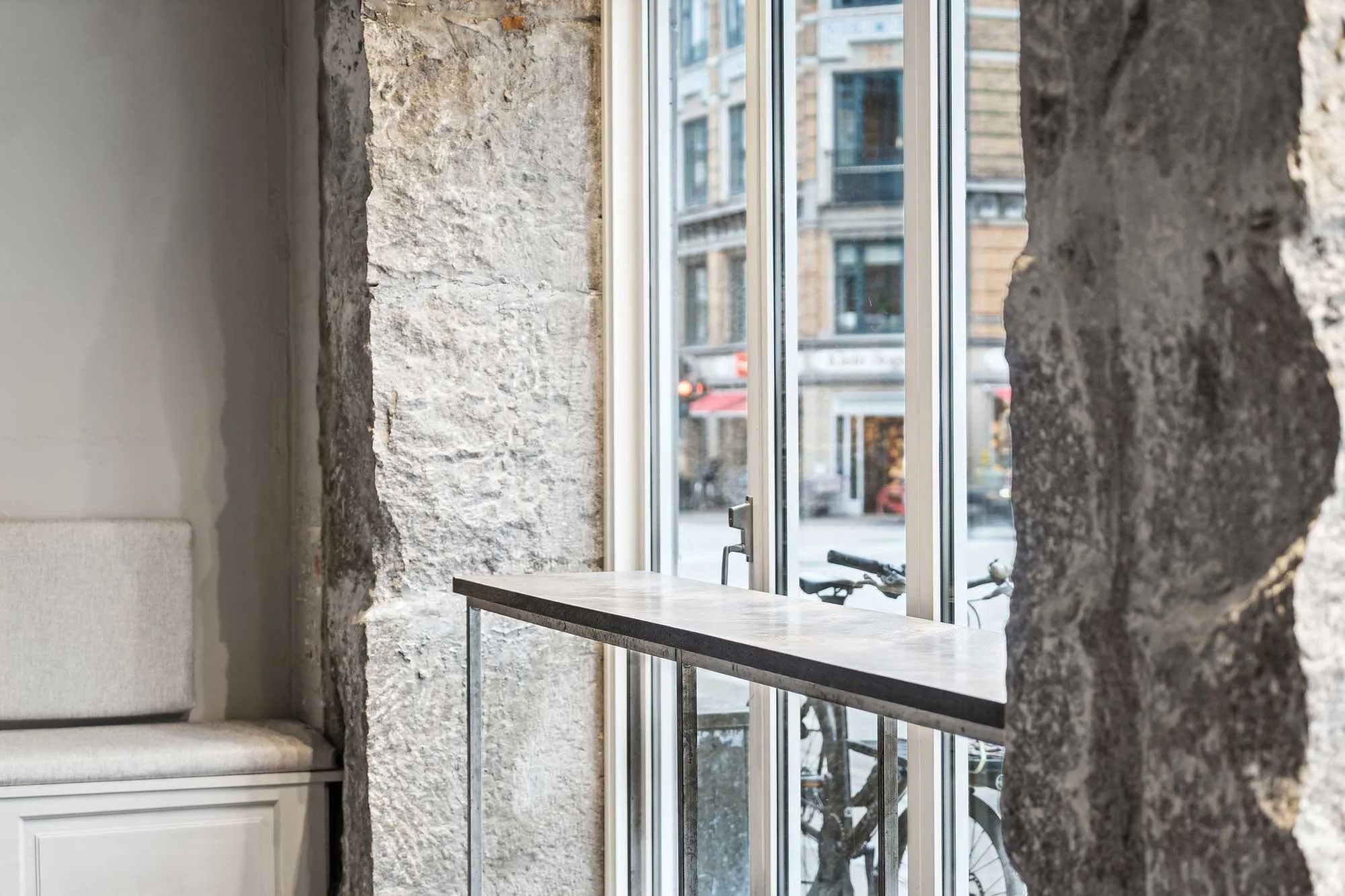 Moderne kontorlokaler med søjle af sten og vinduesfront og metalbord med kontorstole og cykler bag vinduet