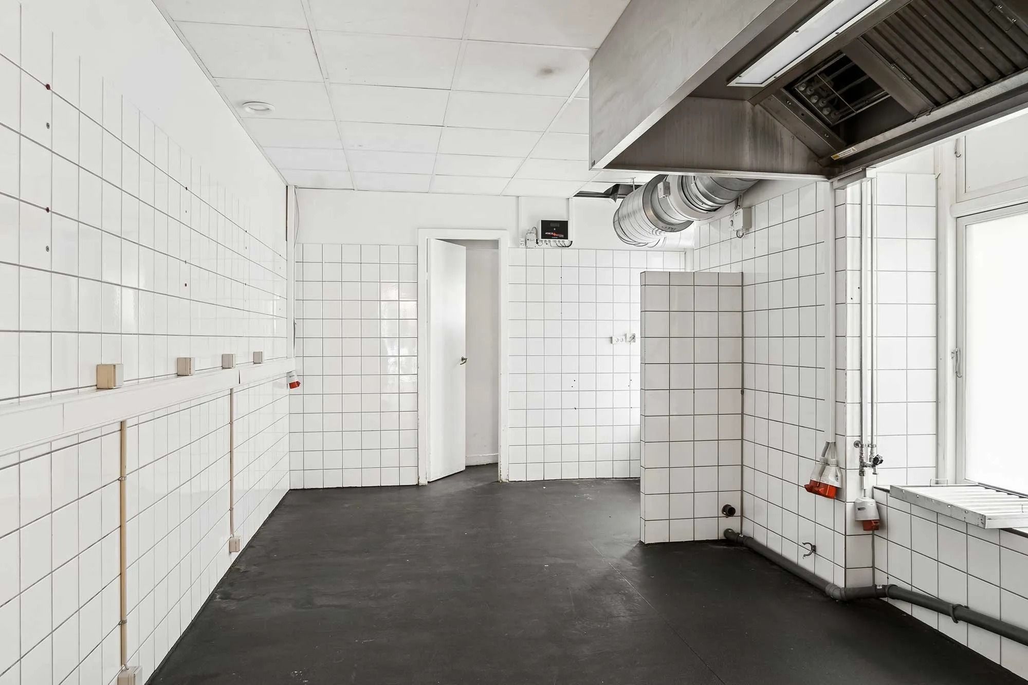 Lokaler med hvide vægge, sort gulv og moderne tekniske faciliteter samt en stor vinduesfront og ventilation