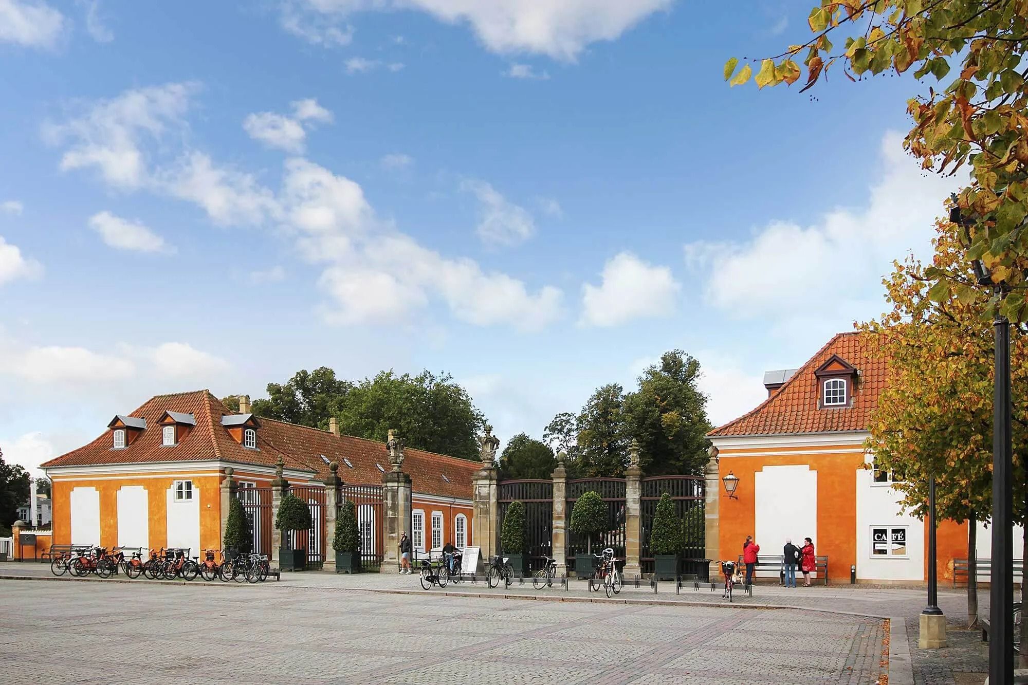 En stor orange og hvid bygning med mange vinduer og træer og blomsterpotter foran en stor port