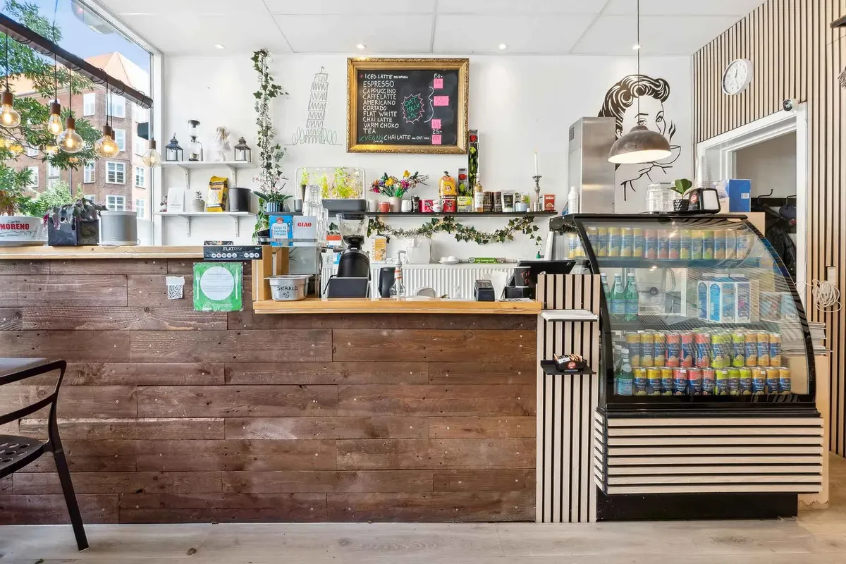 Kaffebar med træbar, glasvæg, menutavle og blomsterdekorationer, indretning med hængende lysekroner og hylder, udvalg af