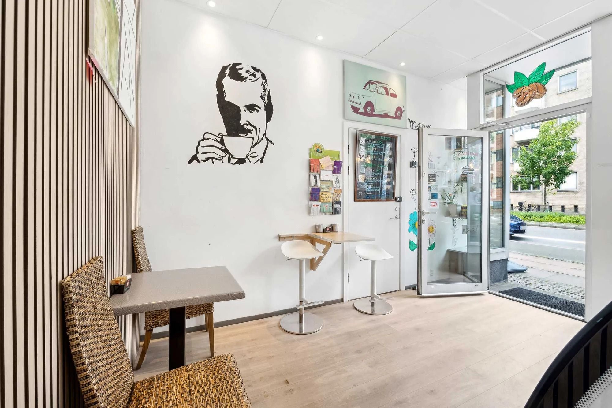 Interiør med højstole og trægulv i hyggeligt café-område med glasdør og udsigt til gågade med cykel og bil