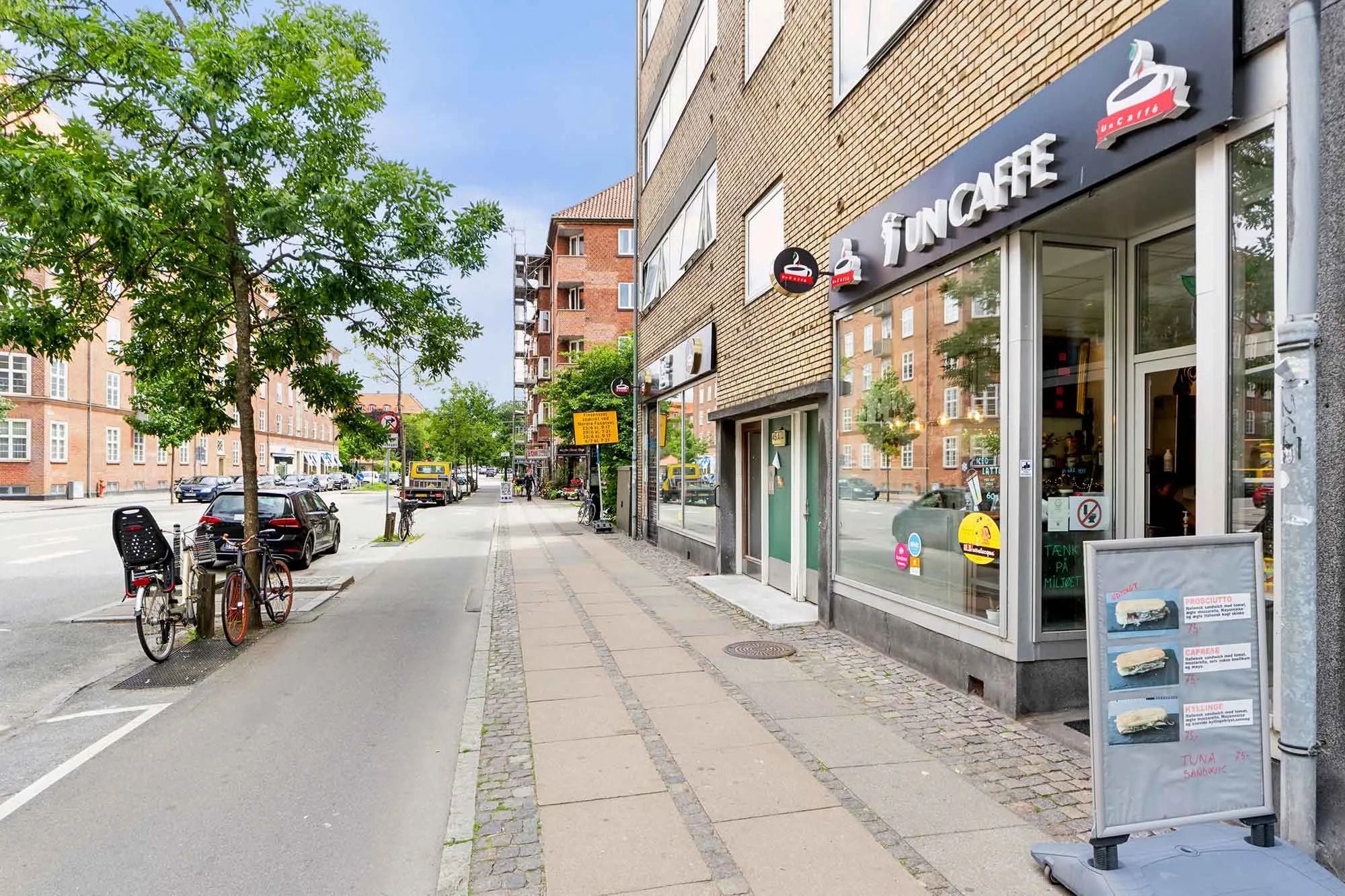 Butikslejemål med cykelparkering og udsigt til Finsensvej med biler og bygninger, herunder caféen Funcaffe