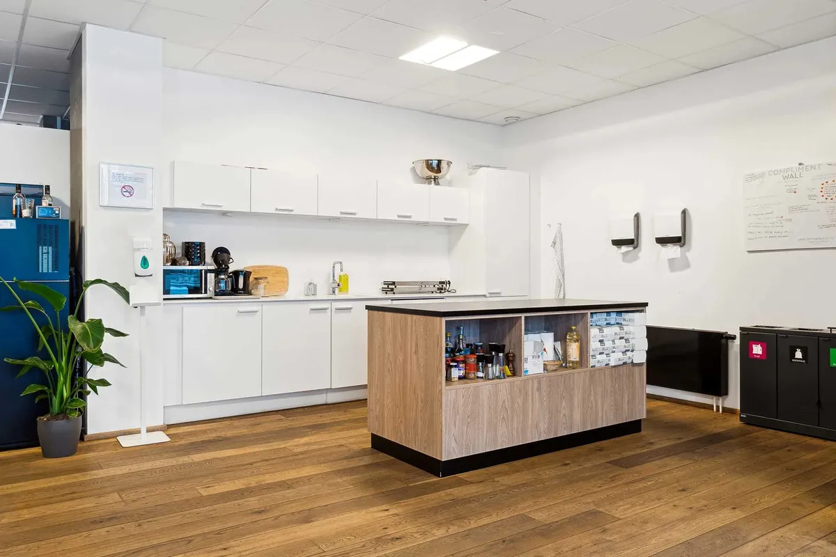 En moderne køkkenhygge med højloft, højloftslys, lyse hvide vægge og en moderne køkkenø med køkkenredskaber og en række