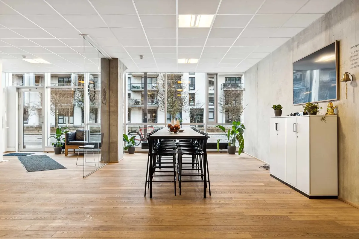 Moderne mødelokale med trægulv, glasvægge, møbler, plantager og en stor tv-skærm på væggen