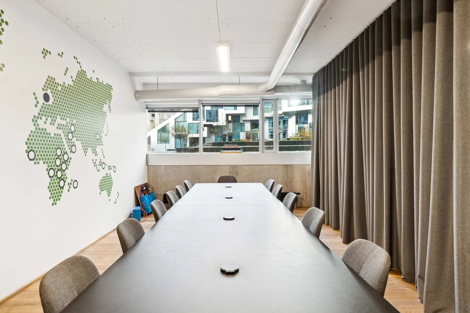 Kontorlokaler med et stort bord, hvor flere stole er stillet op, en væg med et grønt punktmønster og lysegardiner ved vinduet