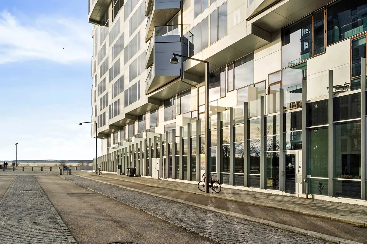 En høj bygning med glasvinduer og metalbøjler parkeret cykel og gadevægslampe på hjørnet af gaden