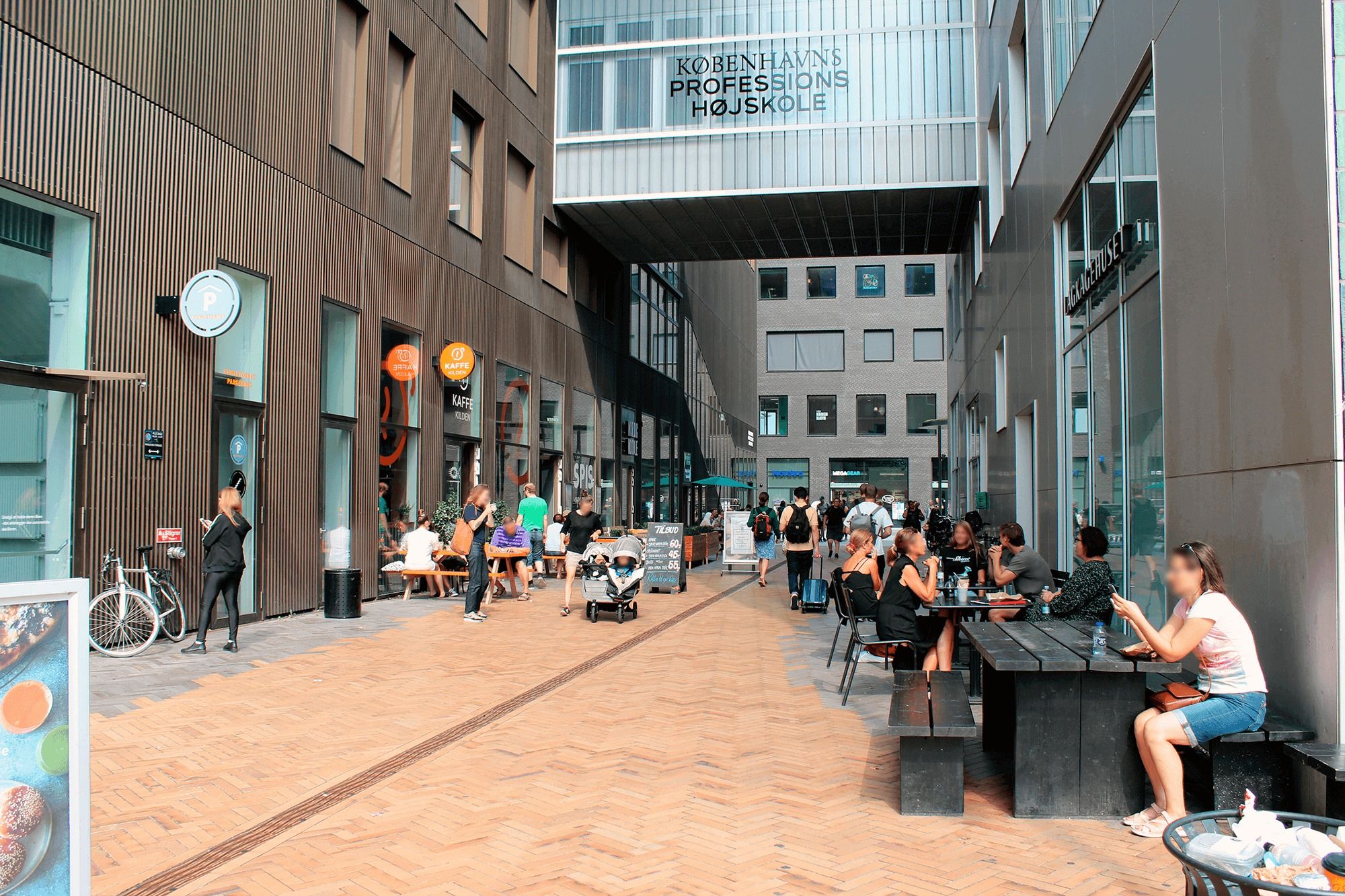 Folk nyder deres morgenmad på en gågade med terrasser og caféer i Carlsberg Byen