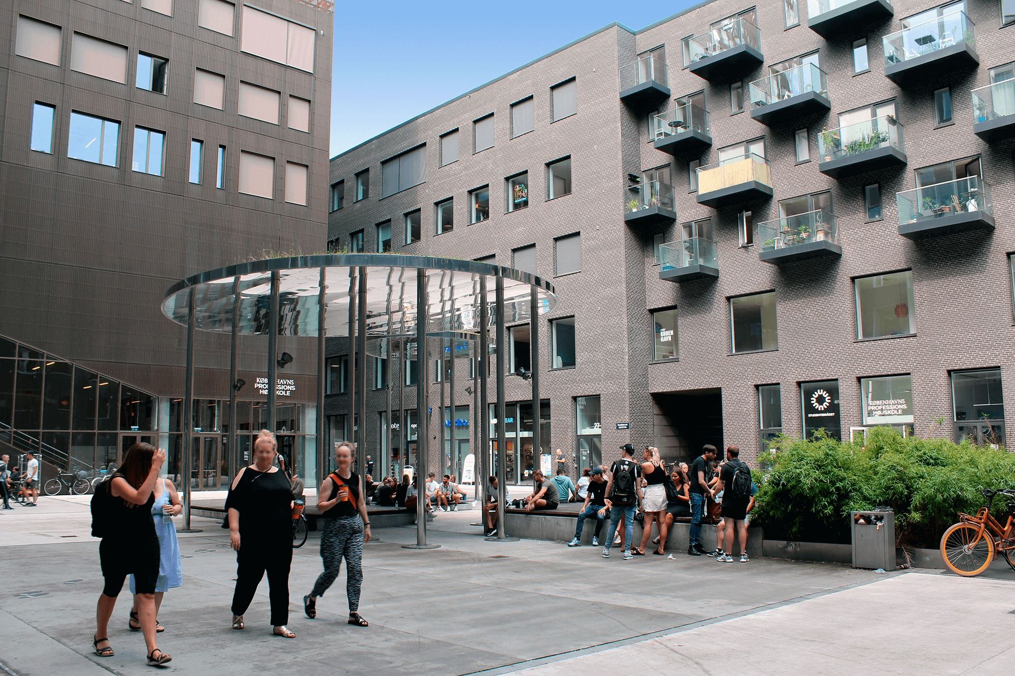 Mennesker går og snakker ved Carlsberg Byens indgangsparti og glaskuppel med plantager og buske, hvor folk sidder på