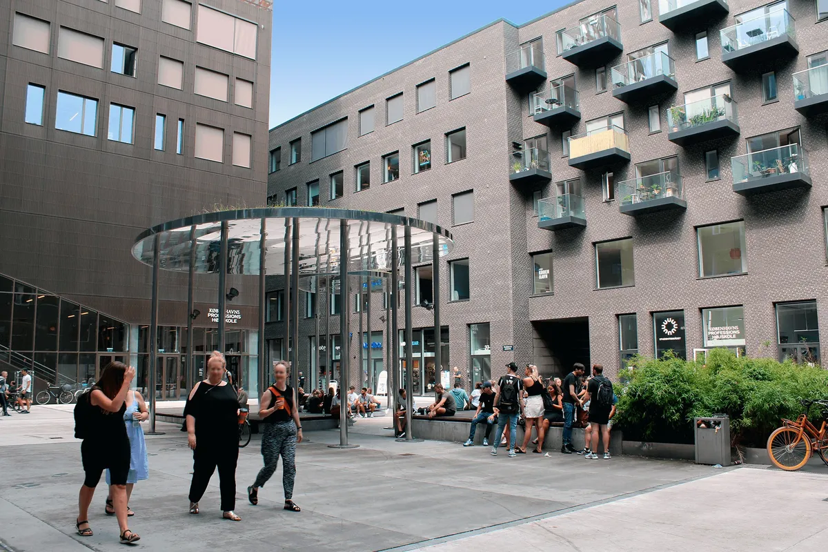 Mennesker går og snakker ved Carlsberg Byens indgangsparti og glaskuppel med plantager og buske, hvor folk sidder på