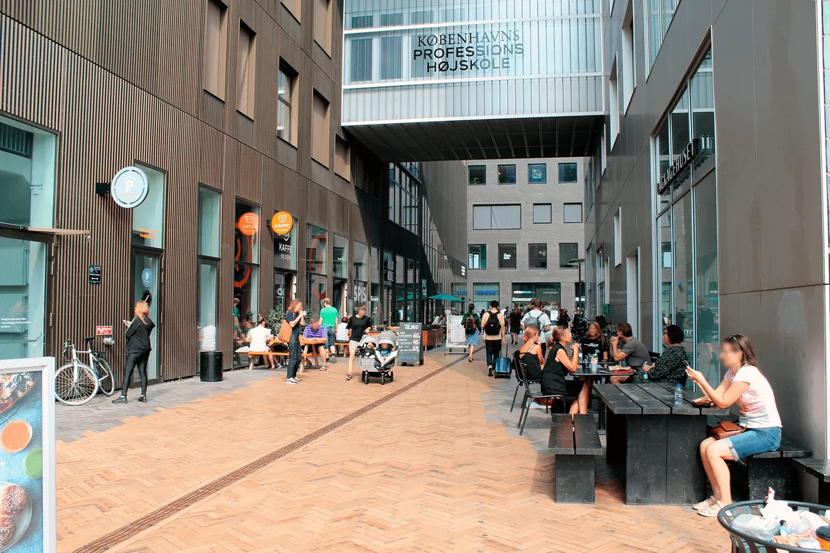 Mennesker samles i en gågade under et skrifttægtsskilt med "Københavns Professionshøjskole" i Carlsberg Byen, hvor folk