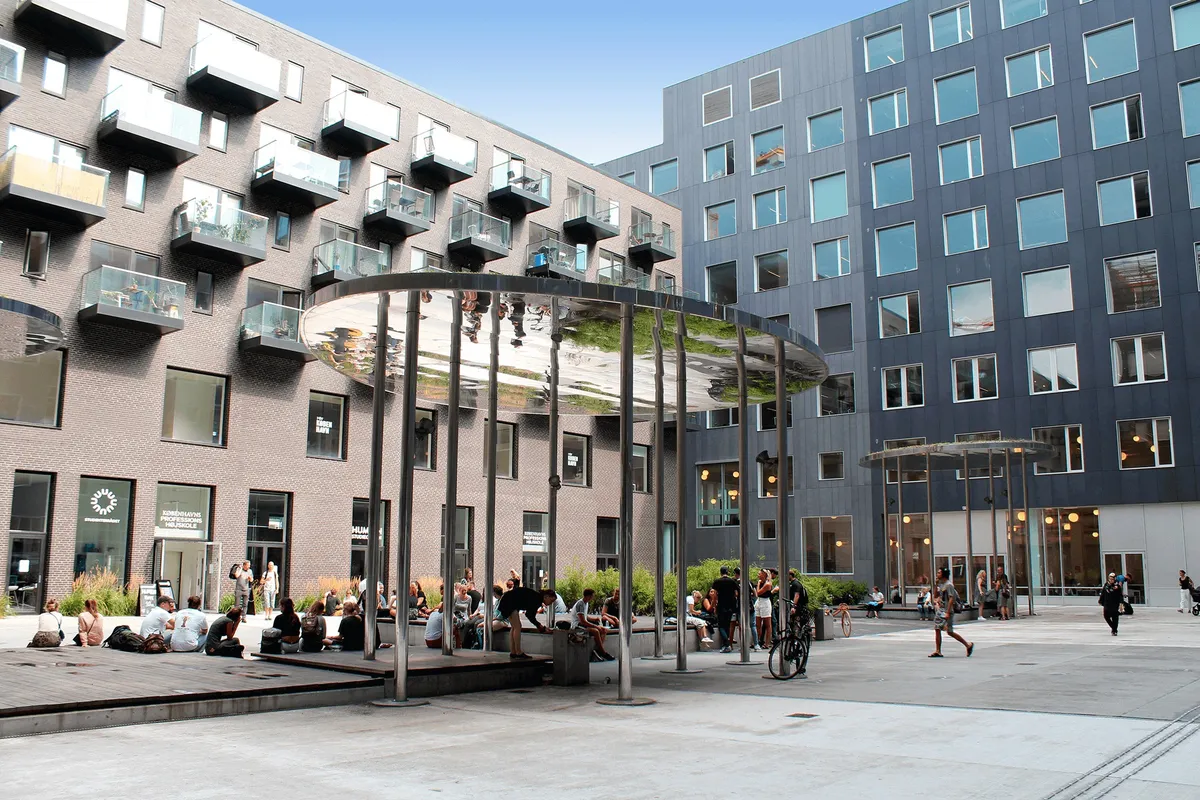 Urbane byrum med moderne bygninger og folk, der slapper af i haven med grønne planter og skulpturer