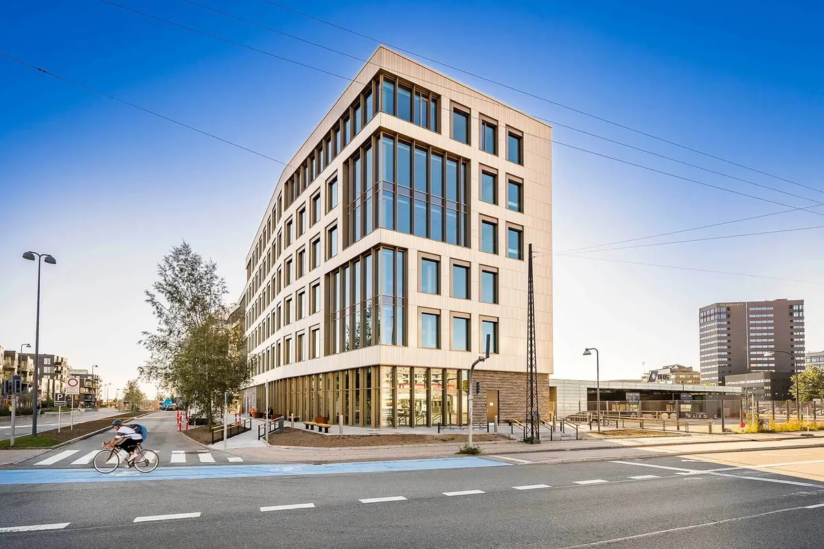 En cykelkører kører på en cykelsti ved en stor bygning med glasvinduer og hjørneplacering i en by