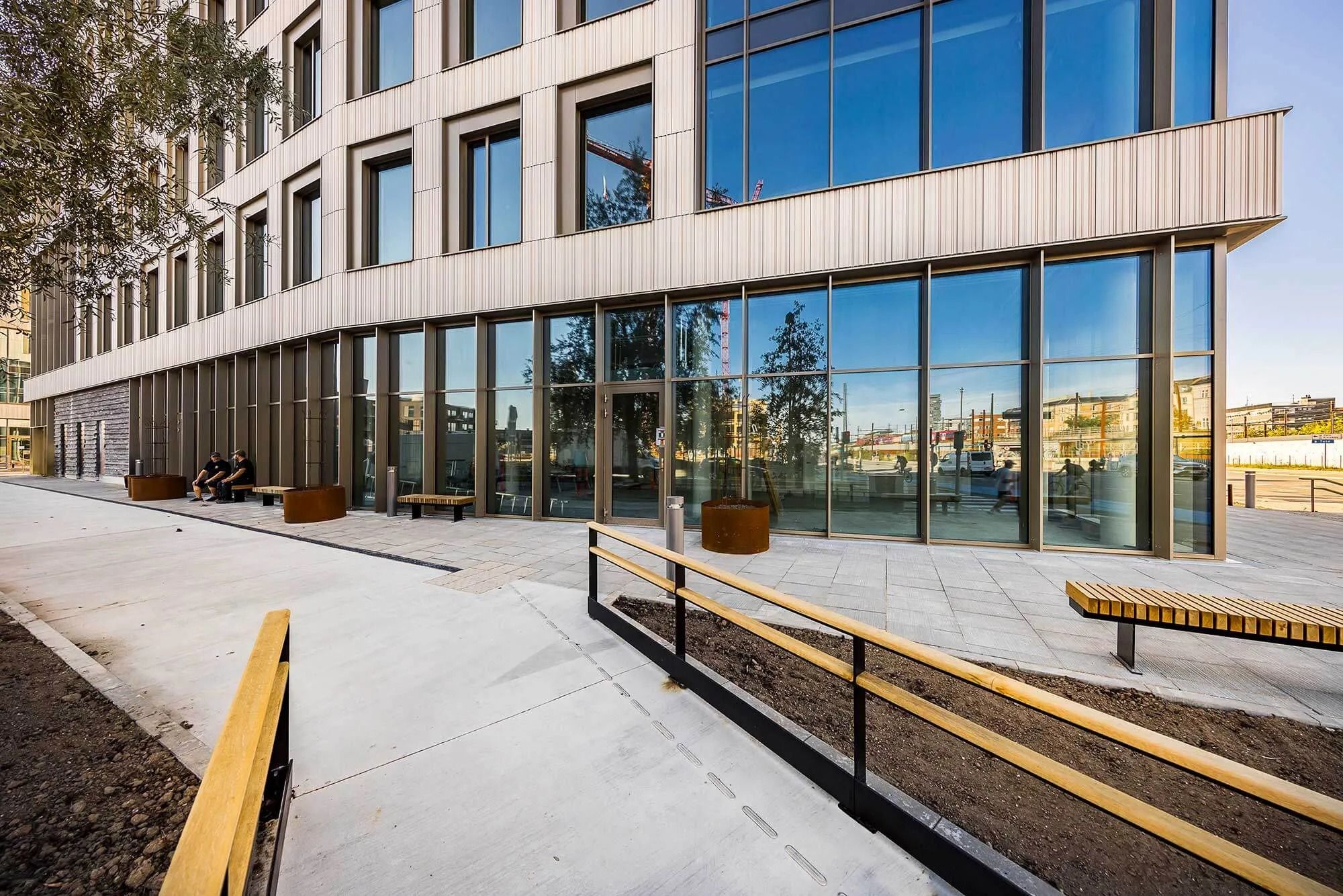 Moderne bygning med glasfasade og træindslag og slanke bænke langs fortovet i en solrig dag