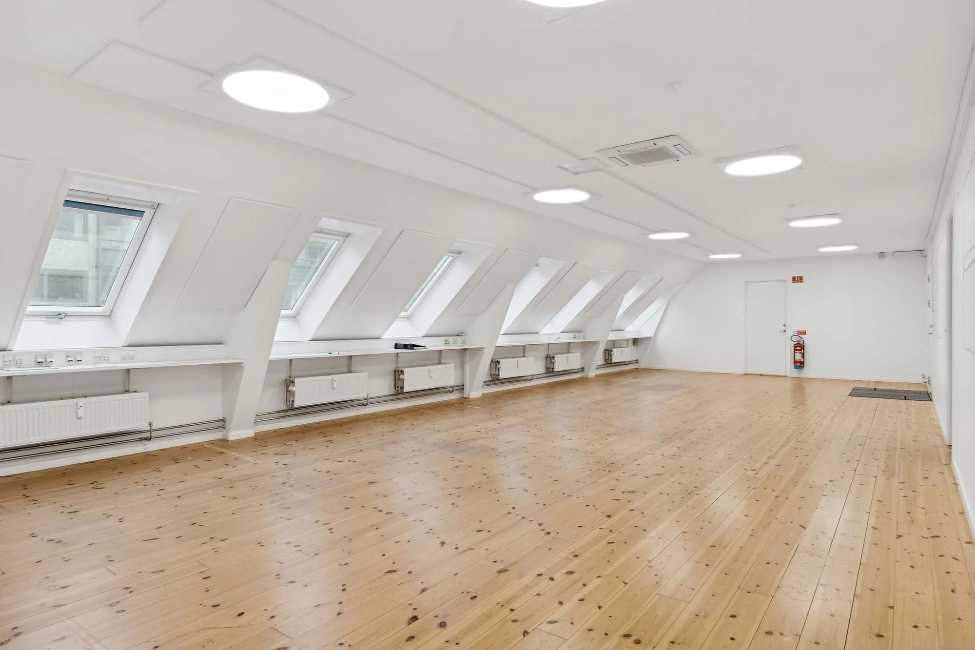 Lejlighed med lyse loftsrum og højloftede rum, hvor gulvet er lavet af træ og loftet er hvidt med runde lys.