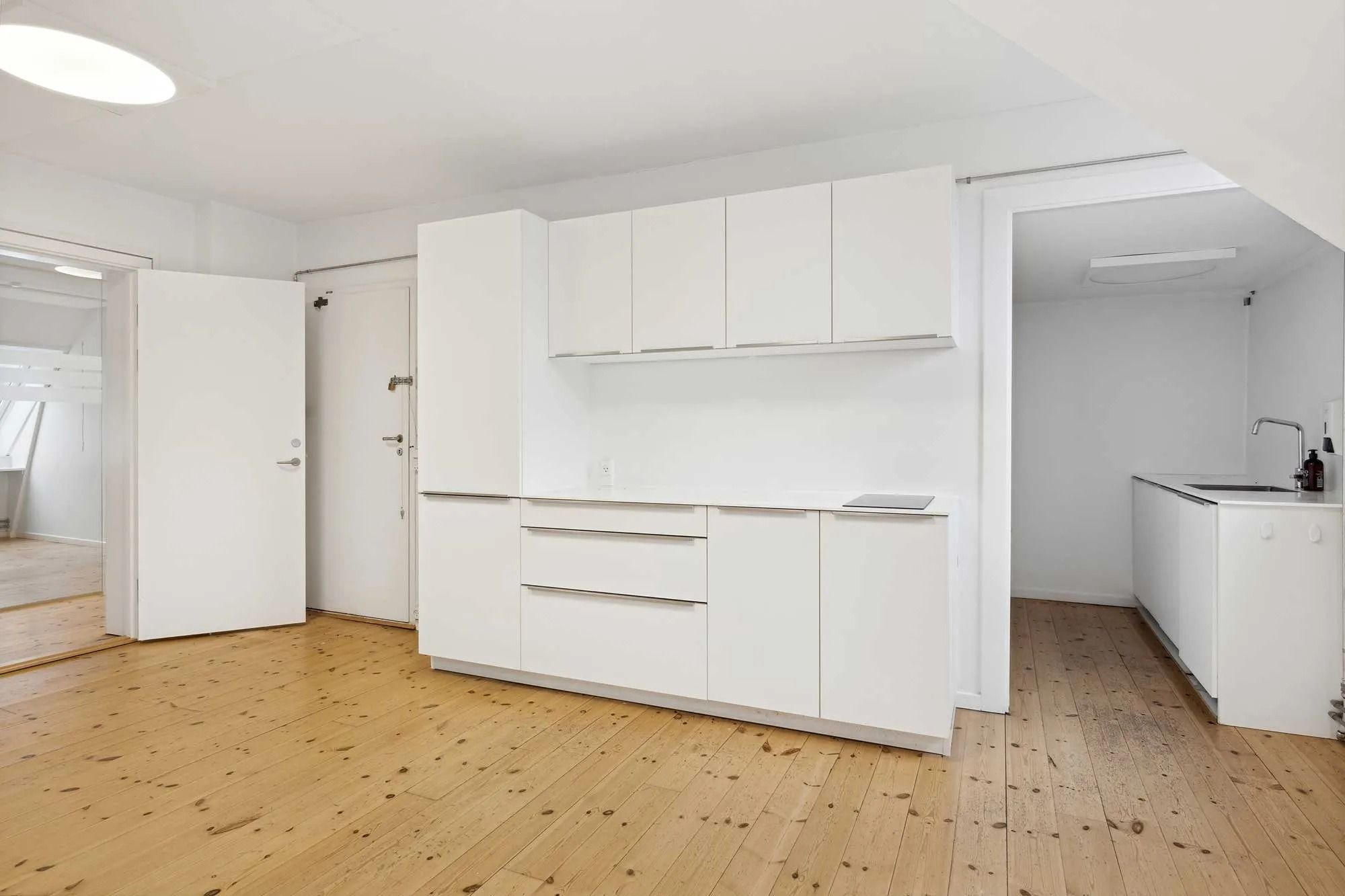 Lejlighed med køkken, hvidt skab og møbler, massivt trægulv og moderne interiørdesign med åbne døre og rum