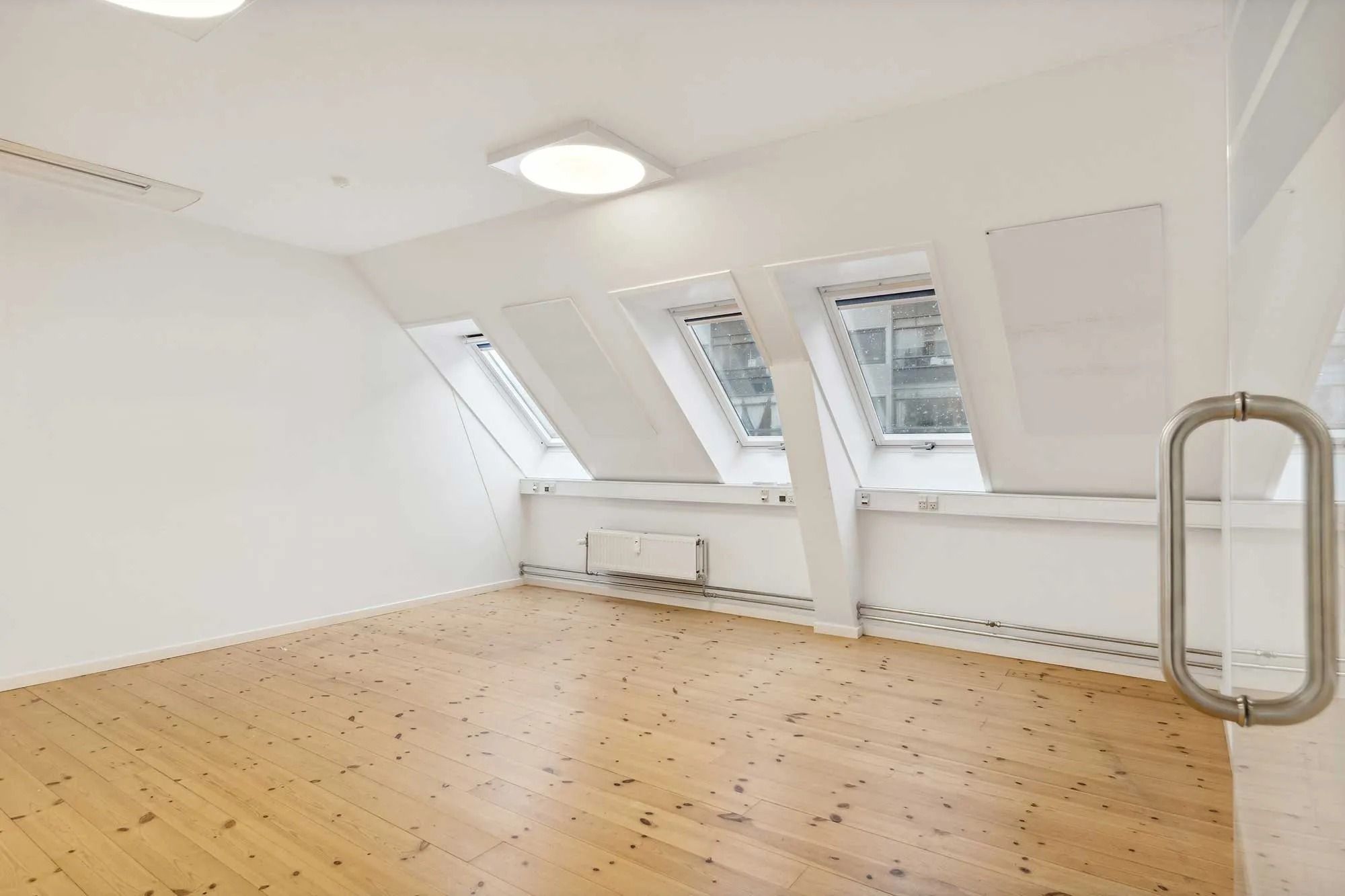 Lejlighed med tre vinduer og lysegul trægulv i et moderne loft med hvide vægge og hvide loft.