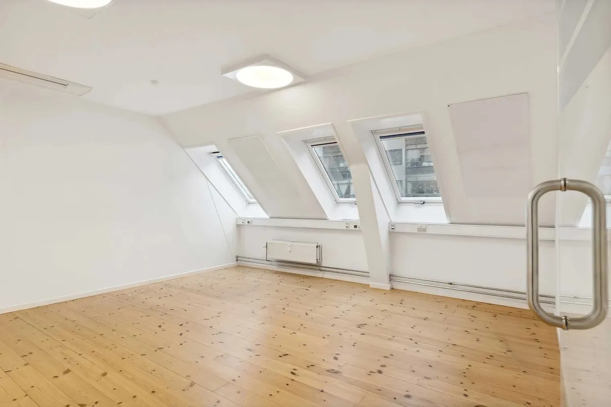 Lejlighed med tre vinduer og lysegul trægulv i et moderne loft med hvide vægge og hvide loft.