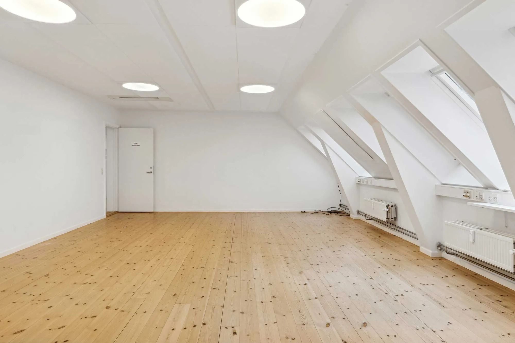 Lejemål med moderne køl og loftsvinduer i ejendom med lyse vægge og trægulv. På væggen er der hvide radiatorer og en hvid