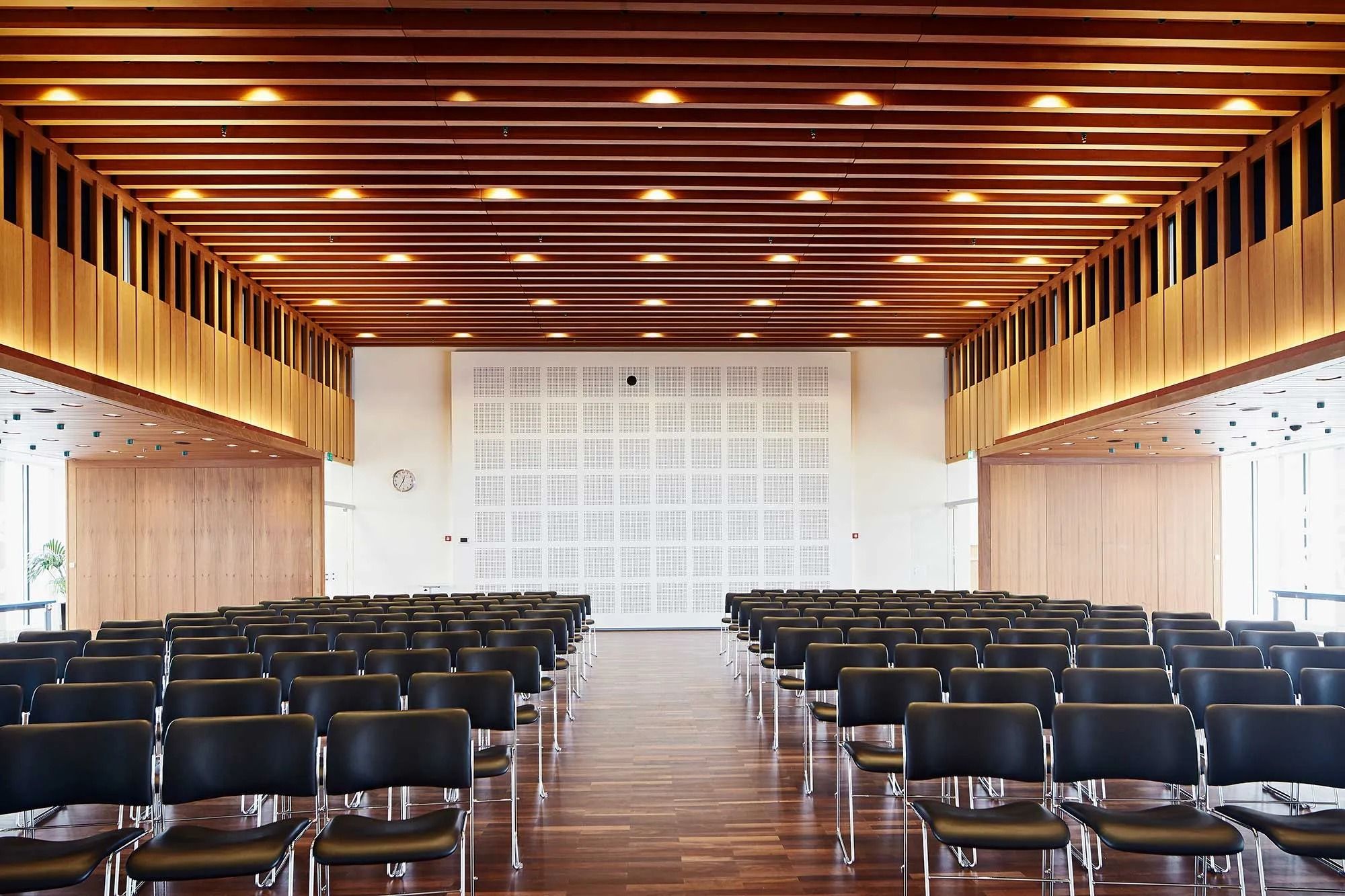 Lyst og pænt konferencelokale med moderne møbler, træpaneler og en hvid væg med akustisk panel og et ur