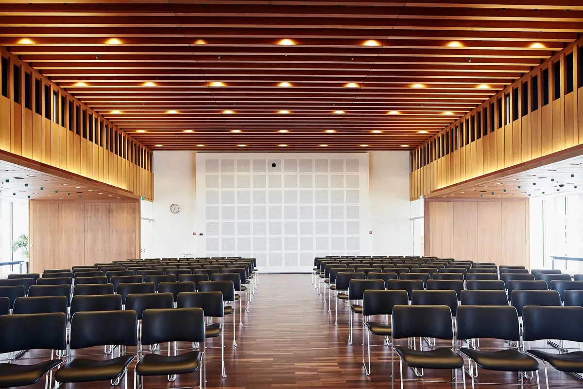 Lyst og pænt konferencelokale med moderne møbler, træpaneler og en hvid væg med akustisk panel og et ur