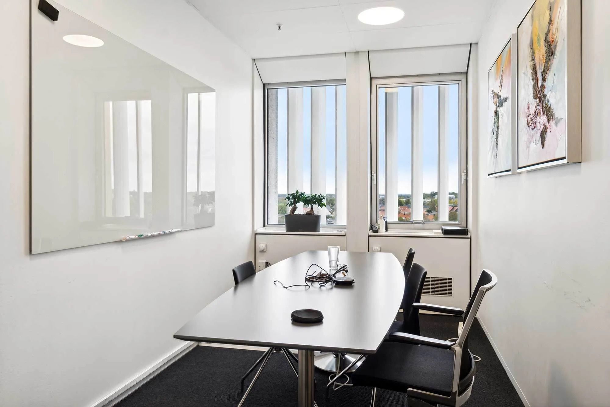 En moderne mødelokale med to vinduer og en stor whiteboard, et plantepotte, og to malerier på væggen