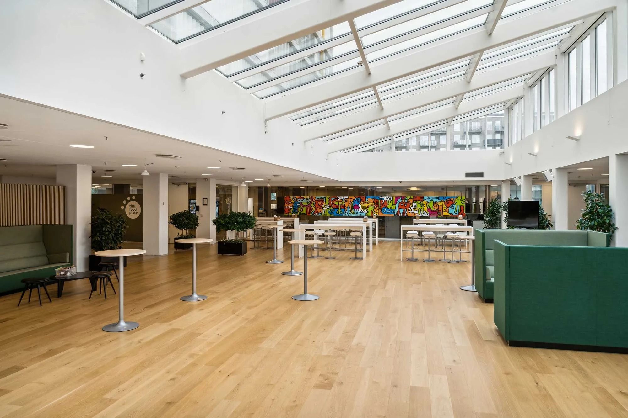 Store åbne rum med lyse lofter, lysegulve, møbler og vægmalerier, samt planteelementer