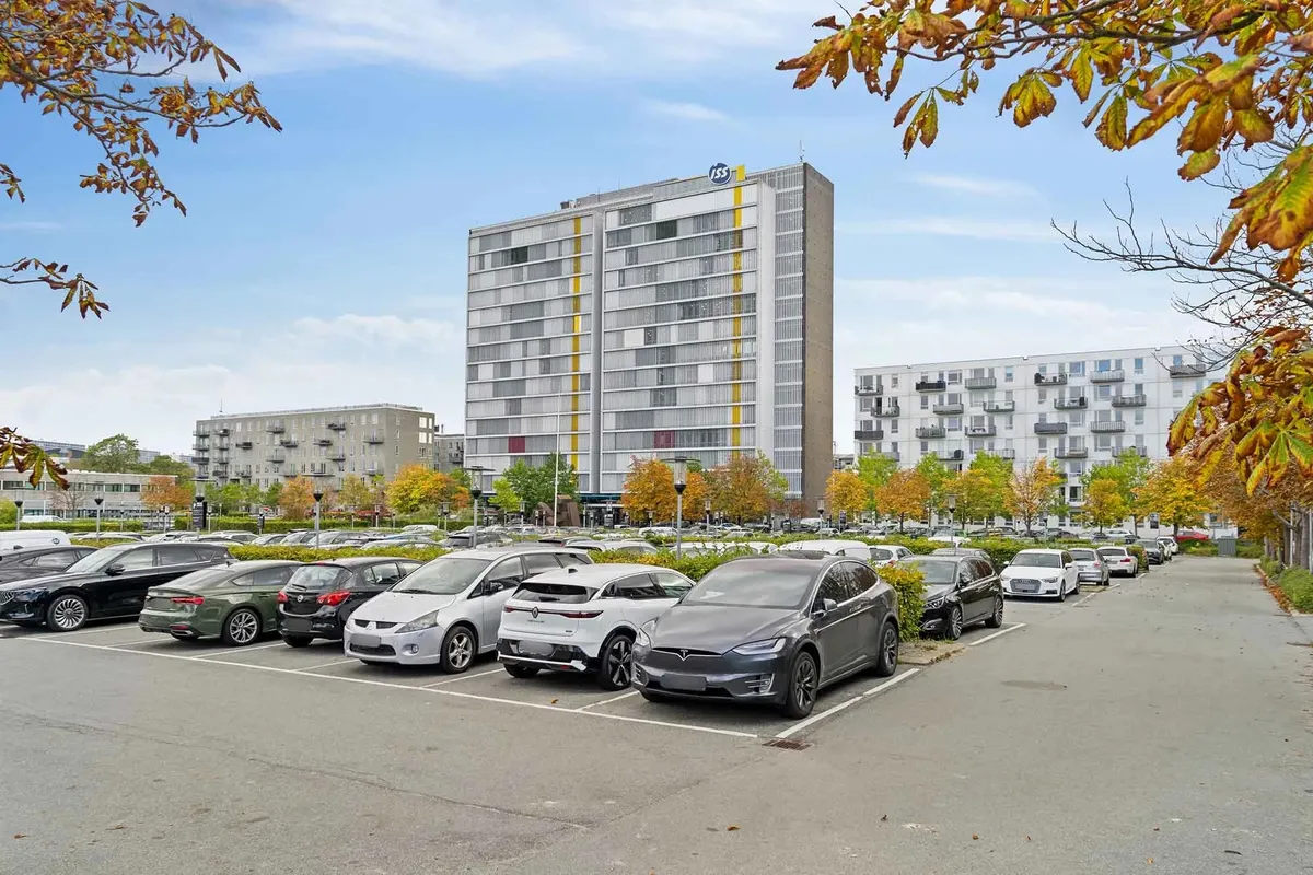 En Tesla Model 3 parkeret i en parkeringsplads med flere biler, med et stort højhus i baggrunden