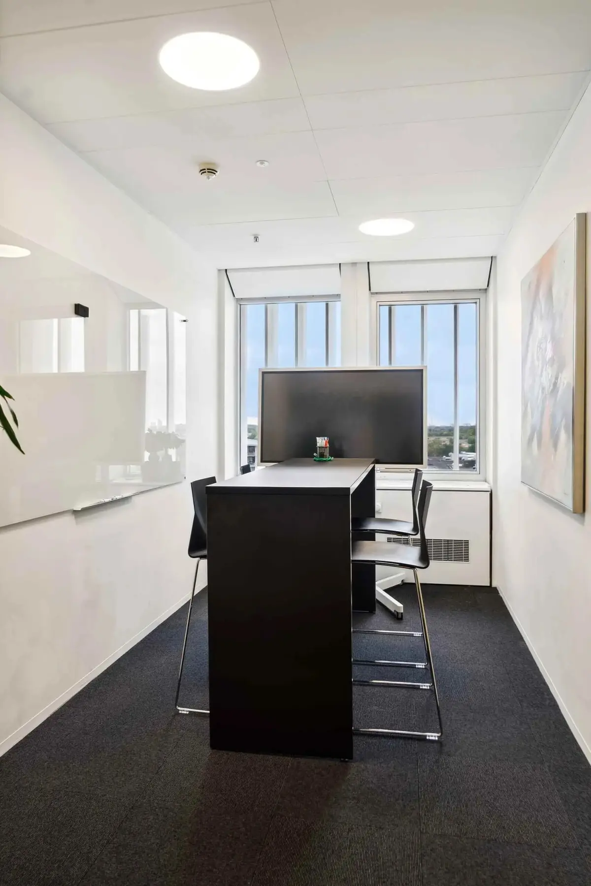 En moderne kontorrum med et stort skrivebord, to stole, et tv, et hvidt tavle og et maleri i hvid ramme