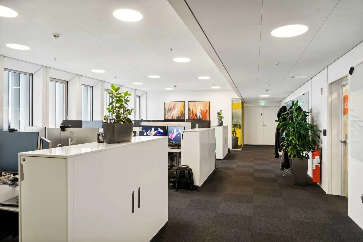 Moderne kontor med højloft og plantepoter med hvide kontormøbler og skærme langs væggen