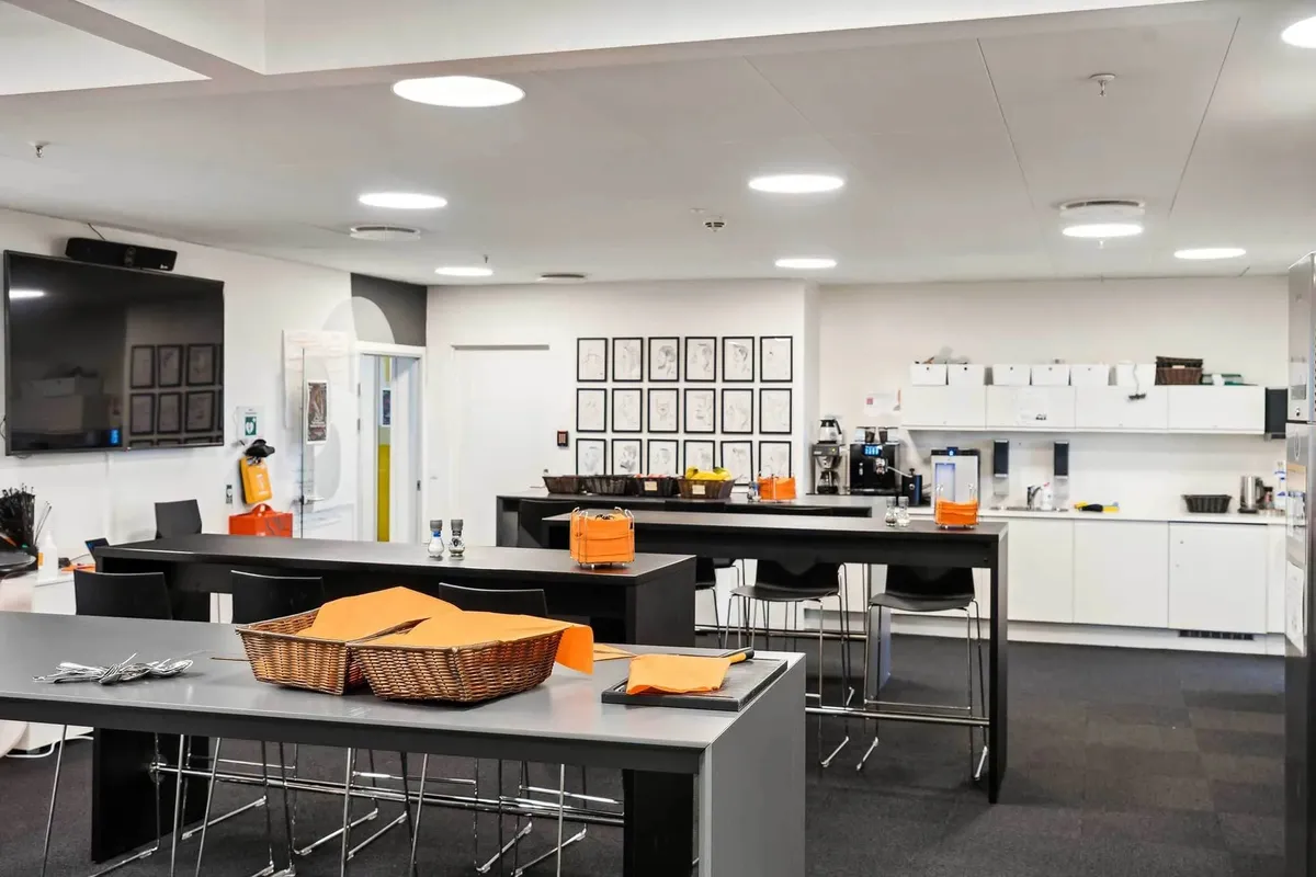 Moderne fællesrum med langtrækkende udsigter, køkken med moderne faciliteter, flere borde og stole, orange servietkurve og