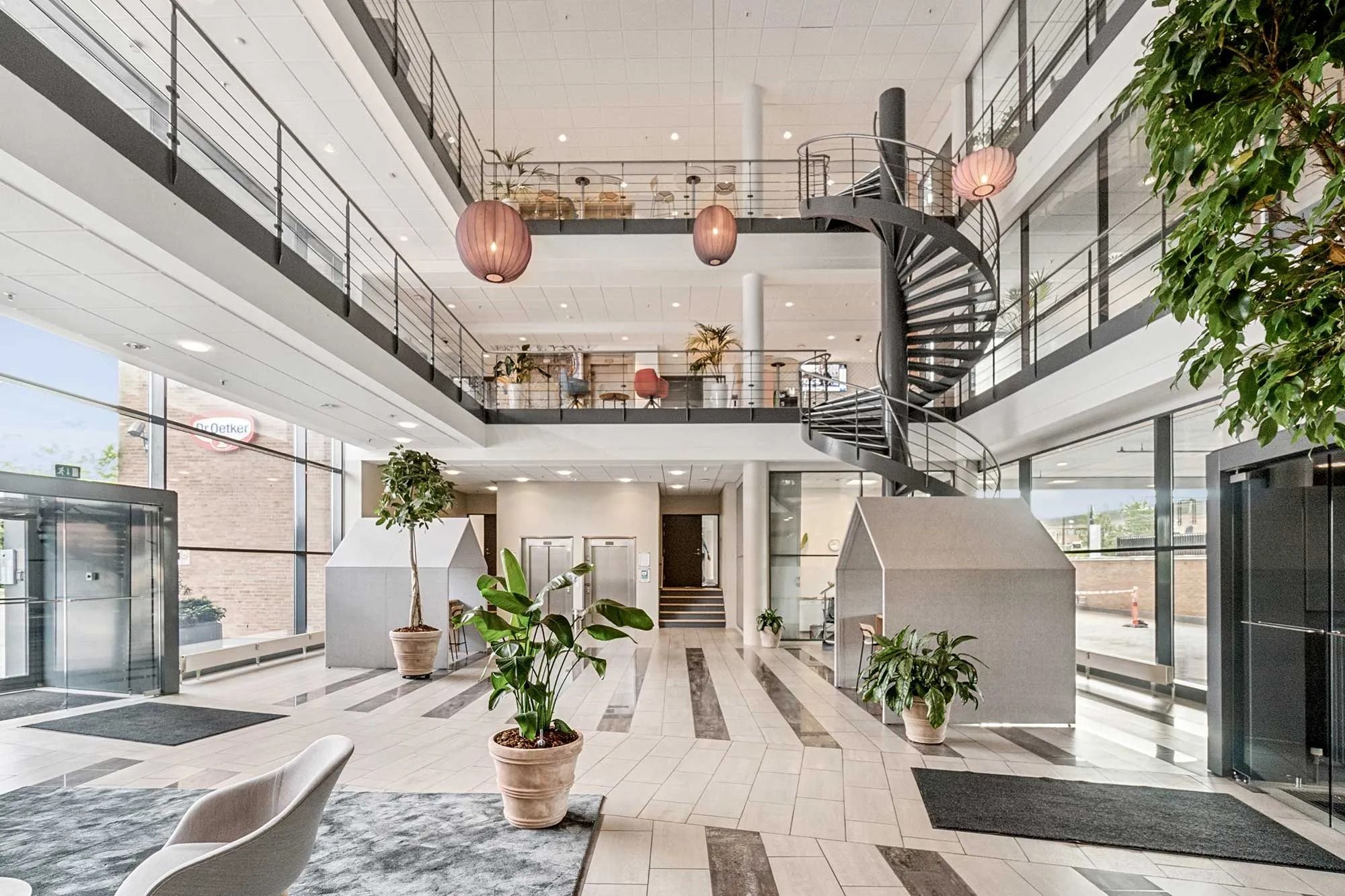 Indgangsparti med moderne møbler og lyse pærekroner i loftet og høj hal med stige og vinduer